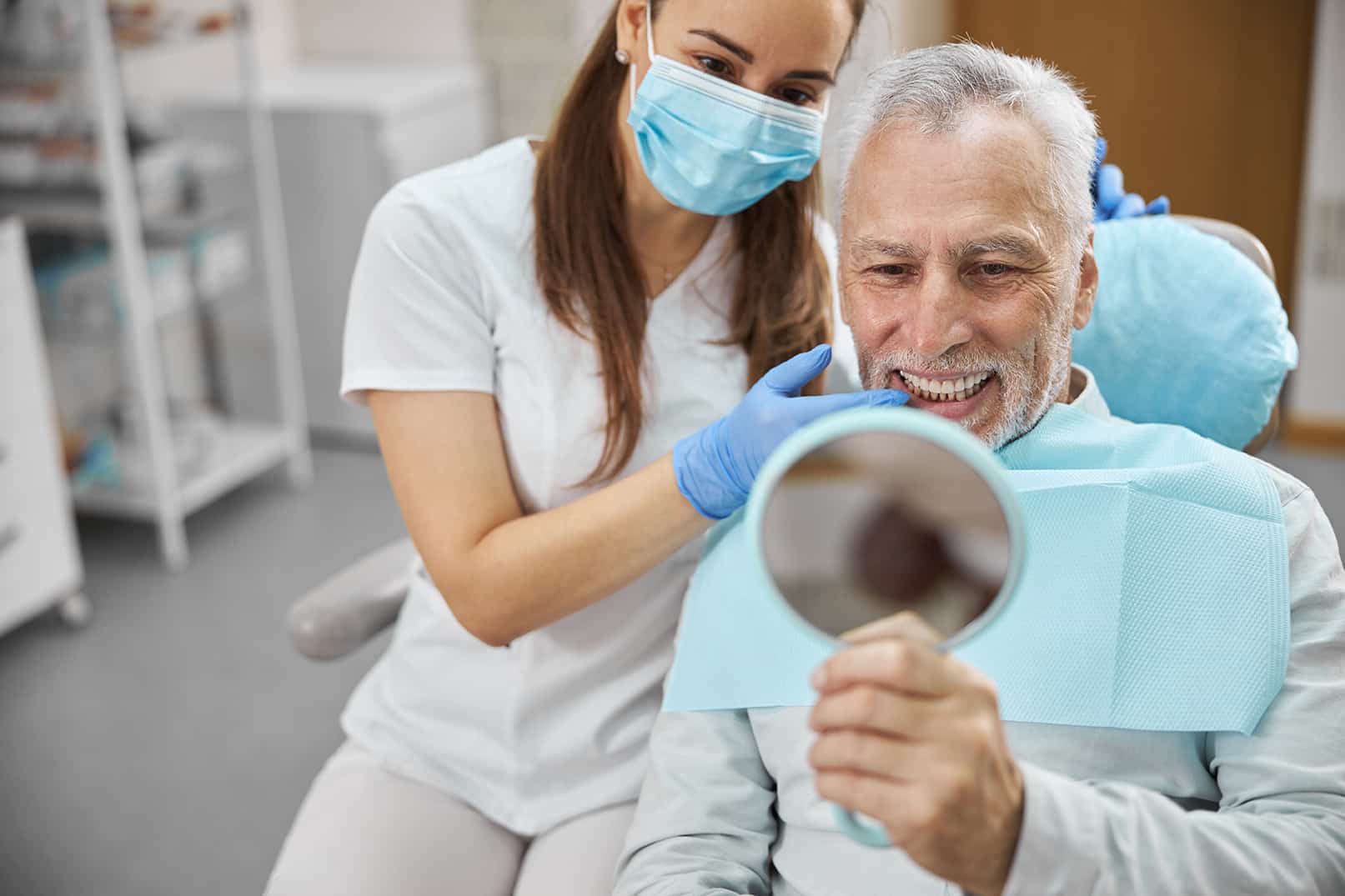 man smiling in mirror talking to dentist during dental implant followup appointment